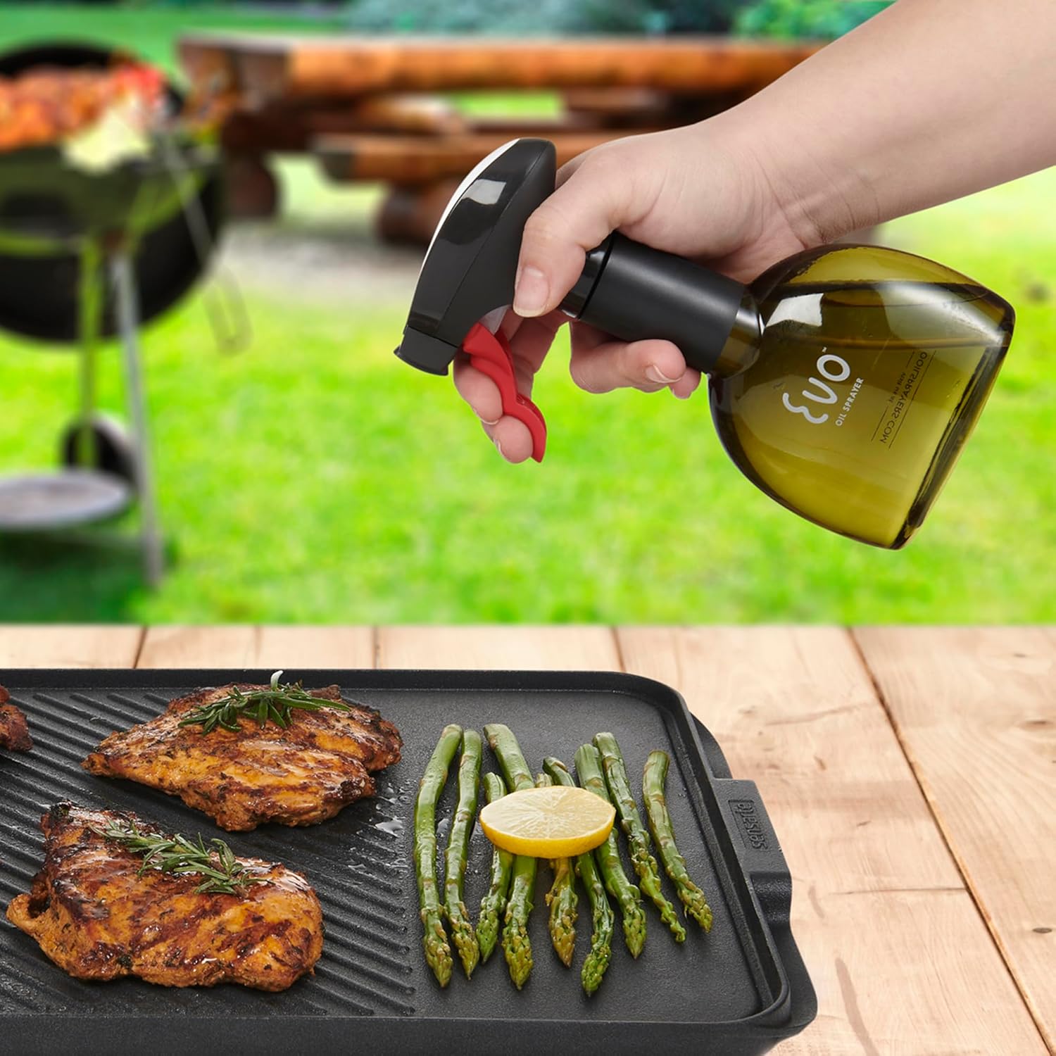 Person using a bottle of olive oil to cook asparagus and chicken on a grill.