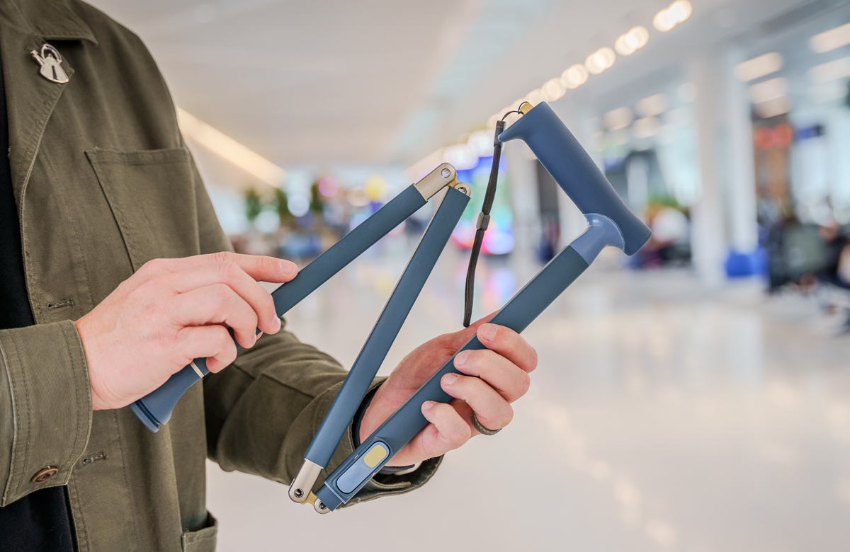 A man's hands holding a slate blue Quick Fold Cane within an mall setting.