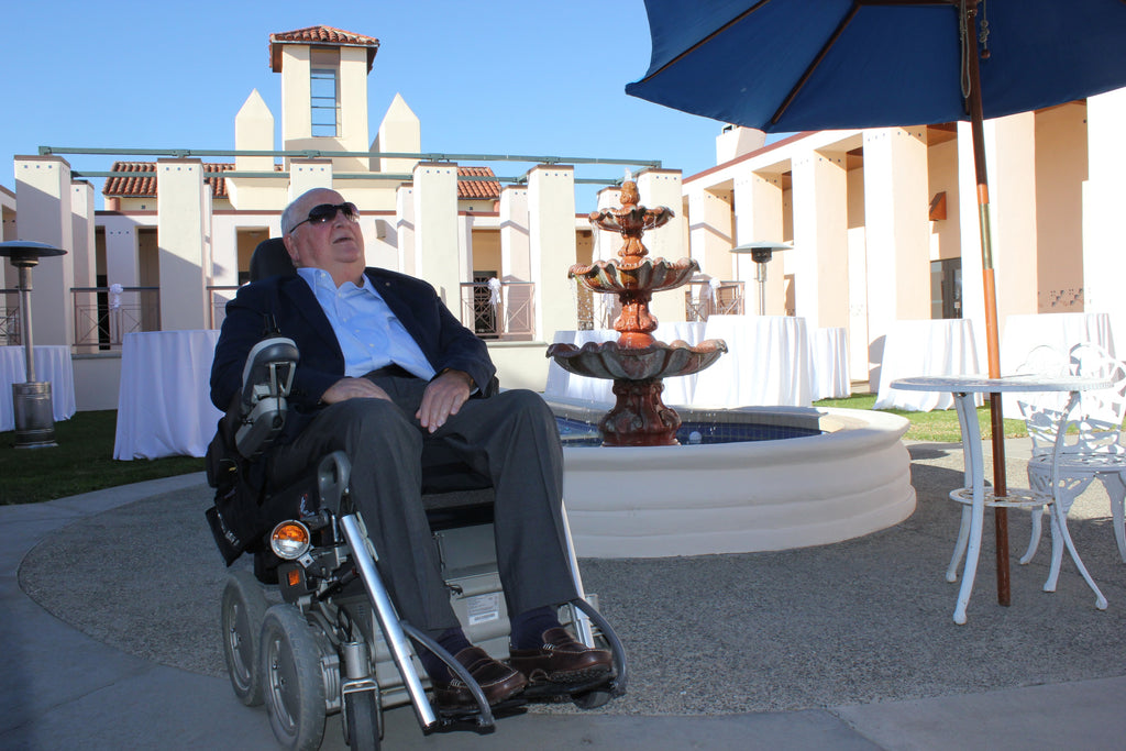 Michael in wheelchair in front of fountain and building wearing sunglasses