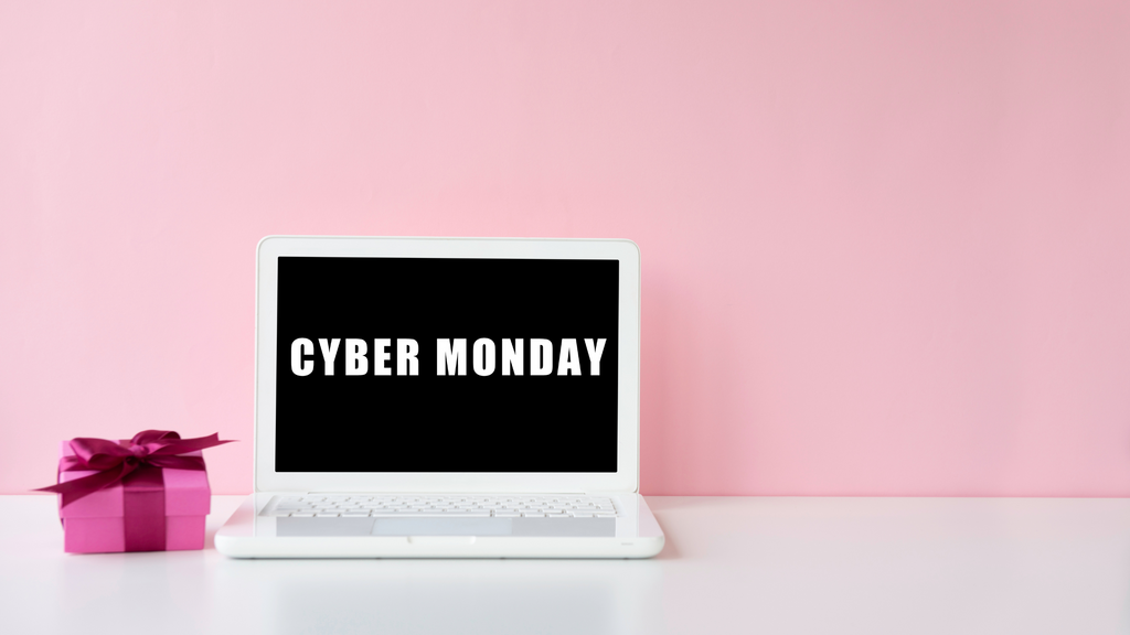 Cyber Monday on computer with pink present next to it and pink wall behind it
