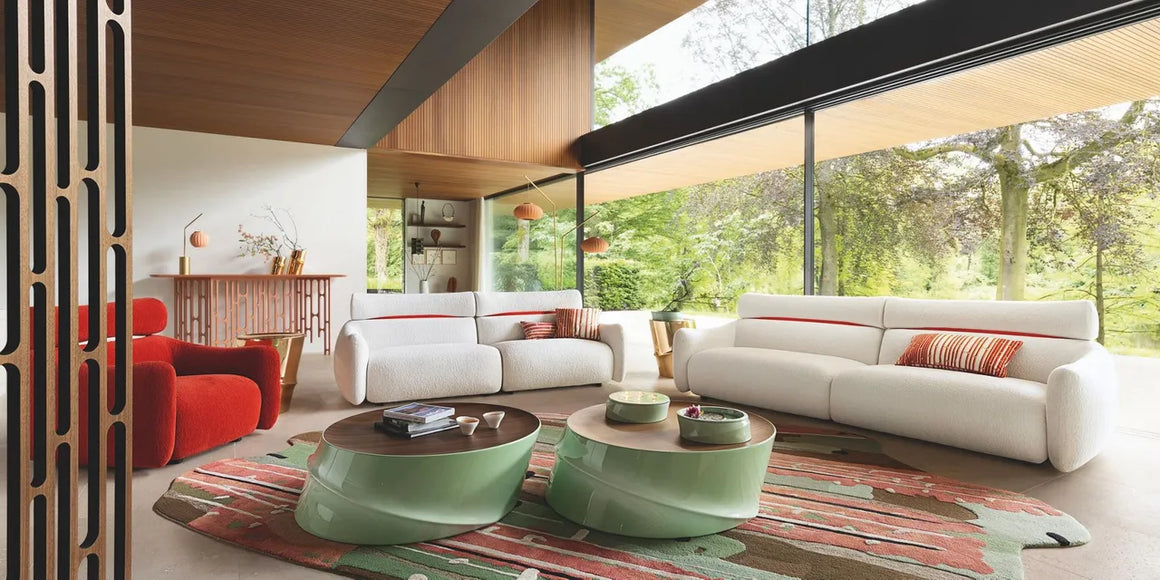 large window room with two white couches with red striped pillows, one red hair, two green circle coffee tables, and a multicolored rug