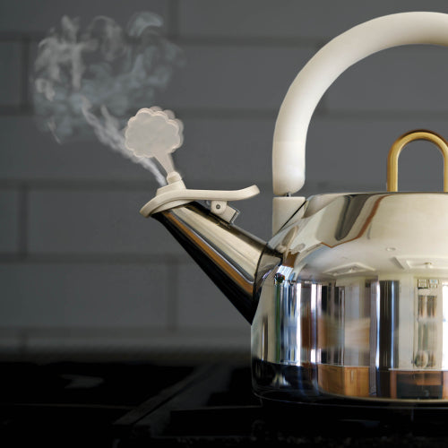 A stainless steel kettle with a white handle and lid, shown on a stovetop with steam rising from the spout against a dark tiled background.