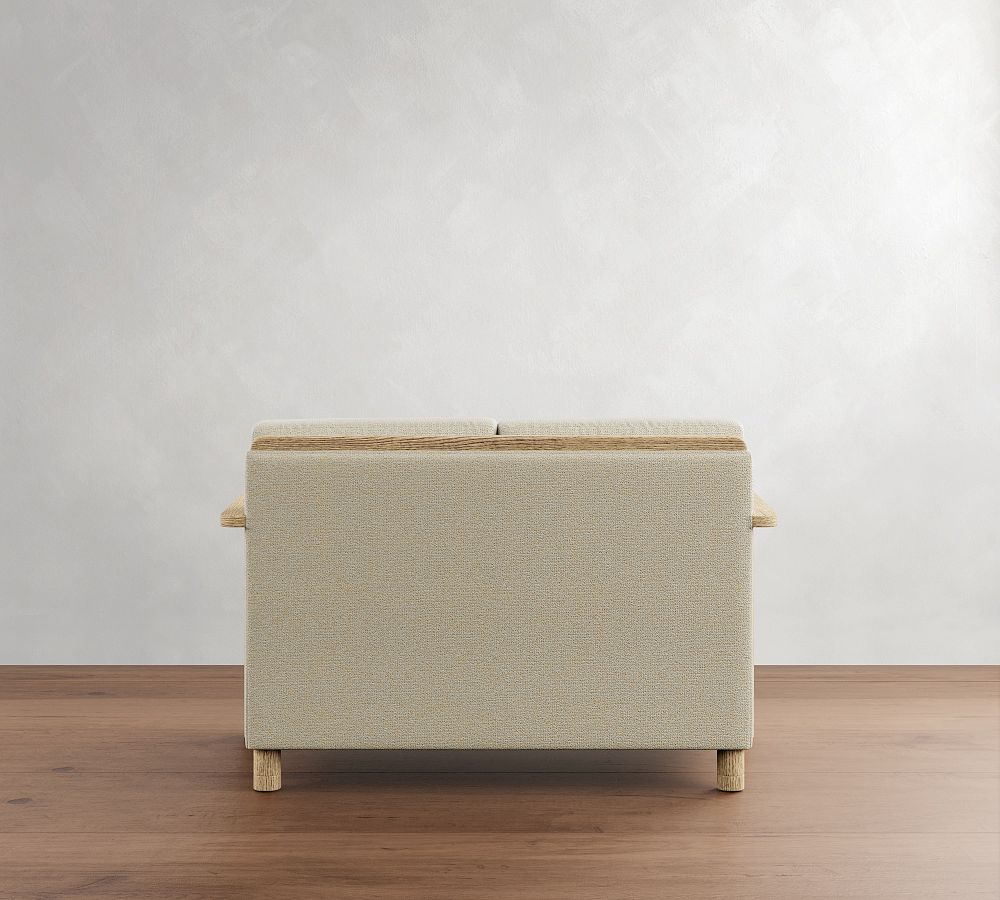 Beige storage bench with wooden legs on a wooden floor against a white wall