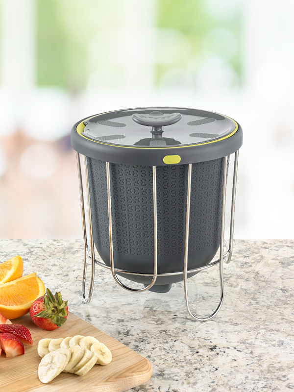 A gray kitchen composter with a black lid and a yellow push-through silicone bucket, placed on a kitchen countertop.