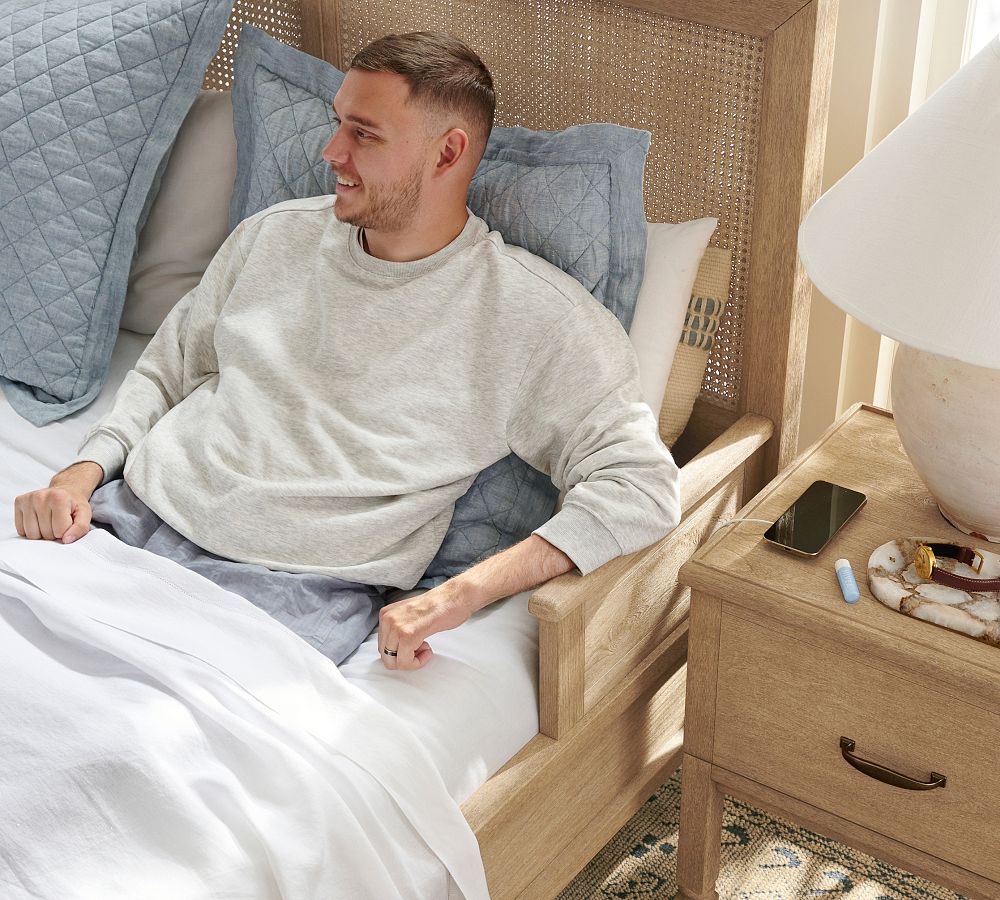 Man sitting on a bed in a bedroom with a nightstand next to him.