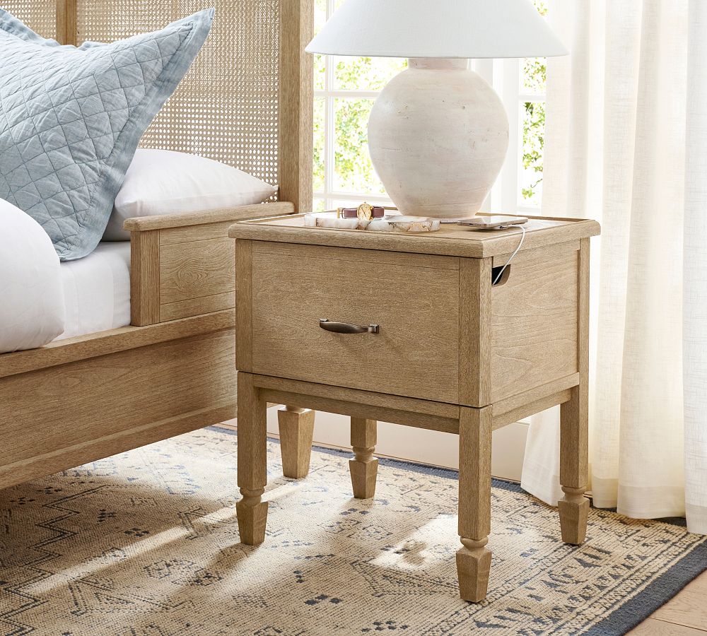 Wooden nightstand with a lamp next to a bed with light blue bedding.
