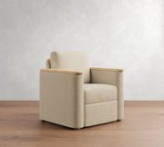 Beige armchair with wooden armrests on a wooden floor against a white wall