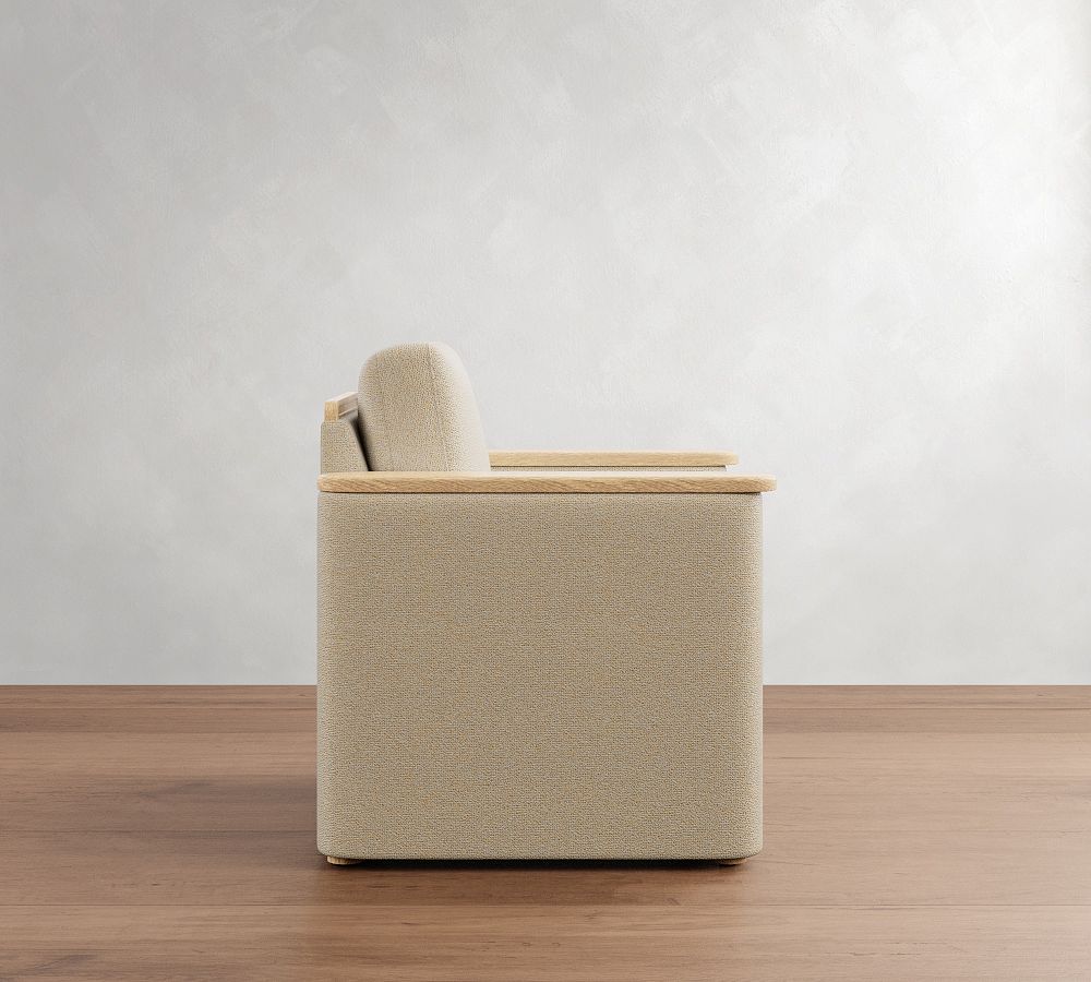 Beige upholstered chair with wooden armrests on a wooden floor against a white wall