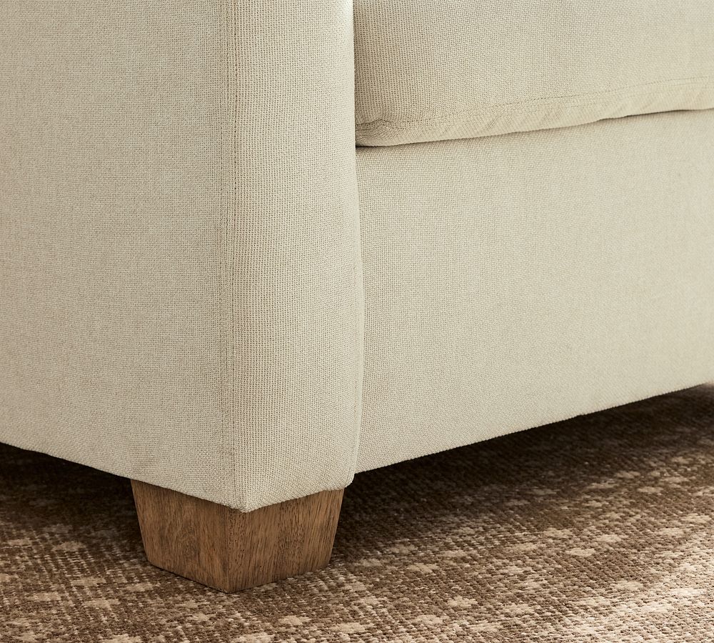 Close-up of a beige upholstered sofa with wooden legs on a textured carpet.